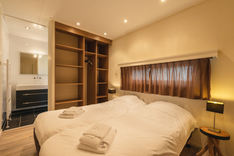 Slaapkamer in Forest Lodge Wellness op Bospark Markelo, Nederland, met tweepersoonsbed, open kast en badkamer.