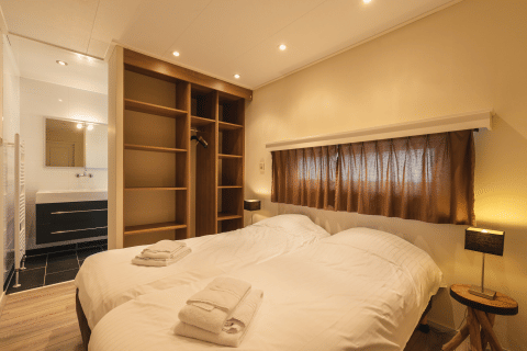 Slaapkamer in Forest Lodge Wellness, Bospark Markelo, Nederland, met tweepersoonsbed, open kast en badkamer.