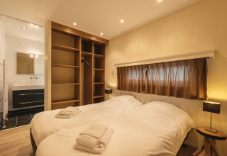 Dormitorio en Forest Lodge Wellness en Bospark Markelo, Países Bajos, con cama doble, armario abierto y baño privado.