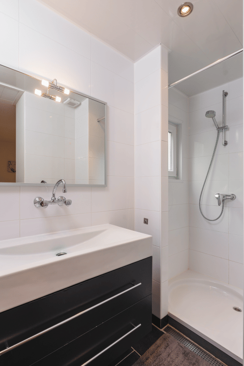 Kleine moderne badkamer met douche, spiegel en zwart meubel in Forest Lodge Wellness, Bospark Markelo.