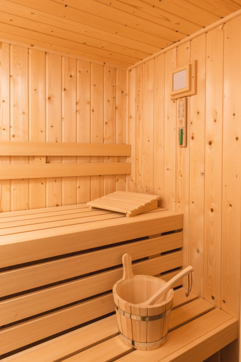 Vista interna di una sauna moderna in legno con panche e secchio al Forest Lodge Wellness, Bospark Markelo.