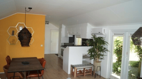 Interior of Lodge Meerkoet at Bospark Markelo, Netherlands, showing a dining area, kitchen, and yellow wall.