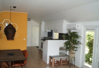 Interno della Lodge Meerkoet al Bospark Markelo, Paesi Bassi: sala da pranzo e cucina moderna e parete gialla.