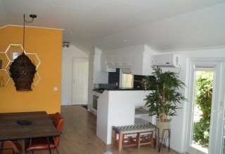 Interno della Lodge Meerkoet al Bospark Markelo, Paesi Bassi: sala da pranzo e cucina moderna e parete gialla.