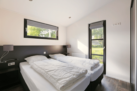 Helles Schlafzimmer in der Lodge Meerkoet, Bospark Markelo, Niederlande, mit zwei Einzelbetten.
