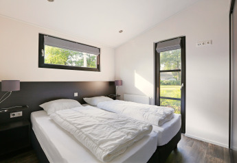 Lichte slaapkamer in Lodge Meerkoet, Bospark Markelo, Nederland, met twee eenpersoonsbedden en ramen.