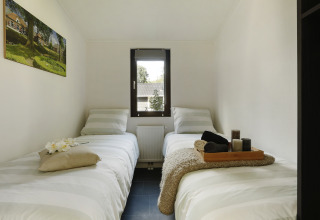 Habitación de glamping acogedora con dos camas individuales, ventana central y decoración moderna.
