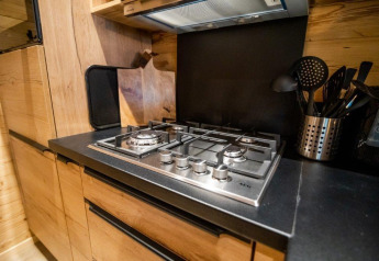 Moderne gaskomfur og sorte bordplader i træbeklædt køkken på Terrace Chalet, Bospark Markelo, Holland.