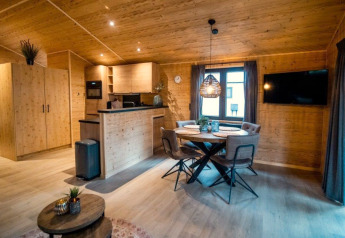 Vista interna di uno chalet in legno accogliente con zona pranzo, TV e cucina moderna al Bospark Markelo.