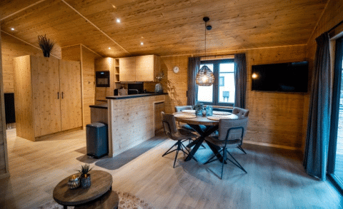 Vista interna di uno chalet in legno accogliente con zona pranzo, TV e cucina moderna al Bospark Markelo.