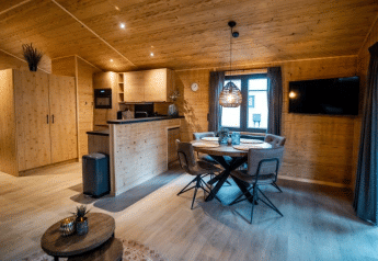 Vista interna di uno chalet in legno accogliente con zona pranzo, TV e cucina moderna al Bospark Markelo.