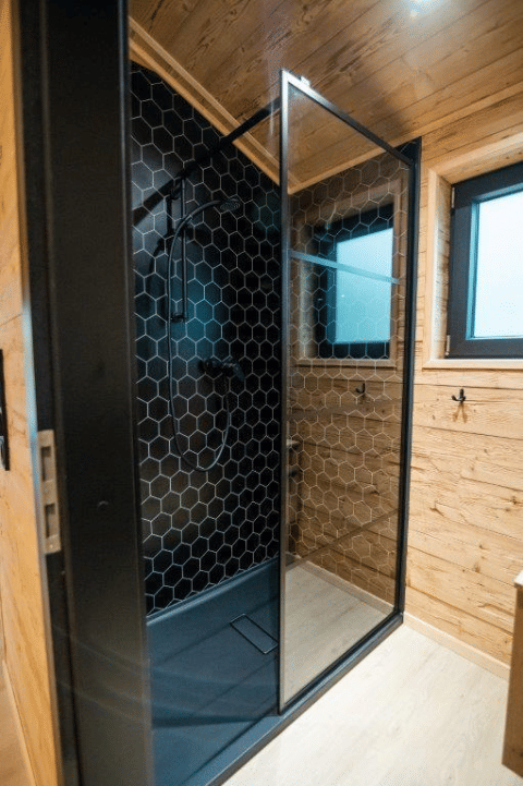 Moderne brusekabine med sort sekskantet flisevæg og træpaneler i Terrace Chalet på Bospark Markelo, Holland.