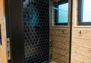 Moderne douche met zwarte zeshoekige tegels en houten muren in Terrace Chalet, Bospark Markelo, Nederland.