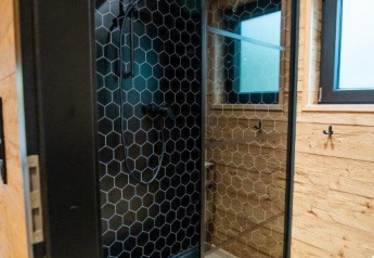 Moderne brusekabine med sort sekskantet flisevæg og træpaneler i Terrace Chalet på Bospark Markelo, Holland.