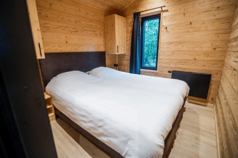 Slaapkamer met houten muren en twee enkele bedden in het Terrace Chalet, Bospark Markelo, Nederland.
