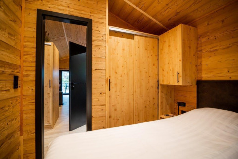 Dormitorio revestido en madera con cama y armario en Terrace Chalet, Bospark Markelo, Países Bajos, estilo moderno.