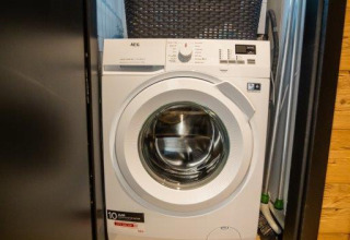 Wasmachine in een kastje met wasmand erop bij Terrace Chalet in Bospark Markelo, Nederland.