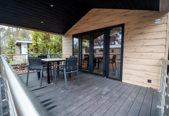 Terrasse mit Tisch und Stühlen am Terrace Chalet im Bospark Markelo, Niederlande, umgeben von Bäumen.