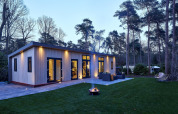 Cubus Lodge en Bospark Markelo, Países Bajos, moderno refugio de madera con terraza al borde del bosque al atardecer.