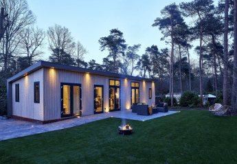 Cubus Lodge en Bospark Markelo, Países Bajos, moderno refugio de madera con terraza al borde del bosque al atardecer.