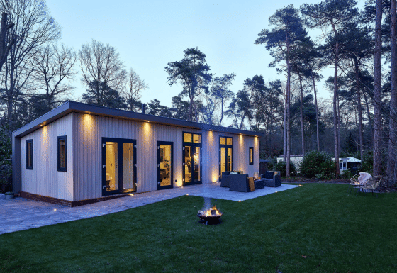 Cubus Lodge im Bospark Markelo, Niederlande, moderne Ferienhütte mit Terrasse im bewaldeten Gelände am Abend.