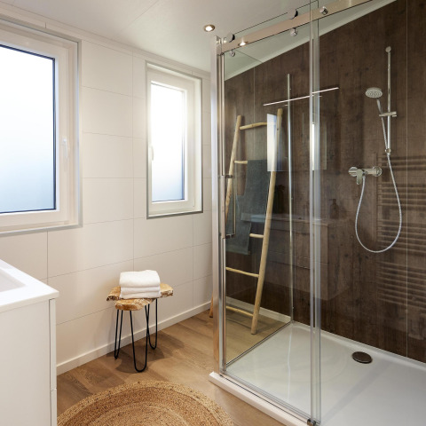 Moderne badeværelse med glasbrusekabine, trævæg, vinduer og minimalistisk indretning på Cubus Lodge.