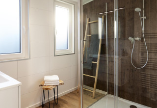 Moderne badeværelse med glasbrusekabine, trævæg, vinduer og minimalistisk indretning på Cubus Lodge.