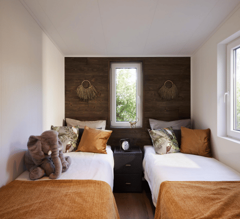 Modernes Schlafzimmer mit zwei Einzelbetten, orangefarbenen Decken und großem Fenster in Cubus Lodge, Bospark Markelo.