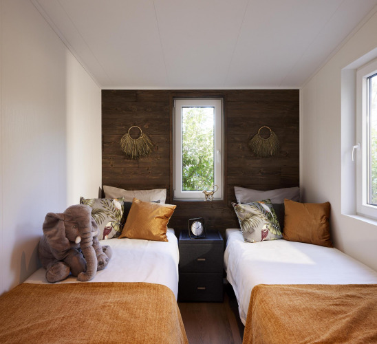 Modernes Schlafzimmer mit zwei Einzelbetten, orangefarbenen Decken und großem Fenster in Cubus Lodge, Bospark Markelo.
