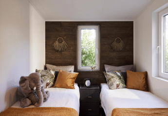 Dormitorio moderno con dos camas individuales, mantas naranjas, peluche de elefante y ventana en Cubus Lodge, Bospark Markelo.