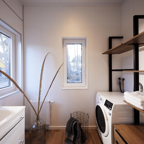 Moderne wasruimte in Cubus Lodge, Bospark Markelo, Nederland, met wasmachine, houten vloer en planken.