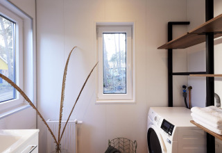 Moderne wasruimte in Cubus Lodge, Bospark Markelo, Nederland, met wasmachine en open houten rekken.