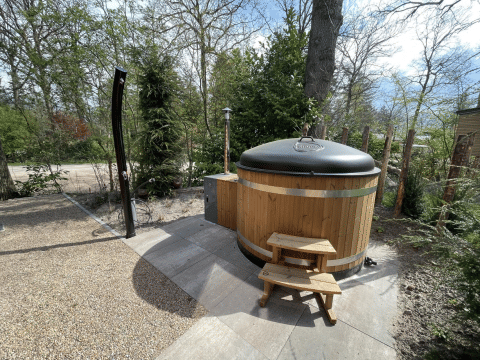 Bain à remous rond en bois avec couvercle et escaliers à l’extérieur d’un lodge à De Utrechtse Heuvelrug, Pays-Bas.