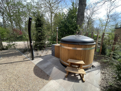 Bañera de hidromasaje redonda de madera con tapa y escalera en el exterior de un lodge en De Utrechtse Heuvelrug, Países Bajos.