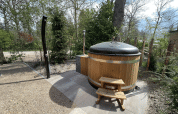 Outdoor photo of a round wooden hot tub with cover and stairs at a lodge in De Utrechtse Heuvelrug, Netherlands.