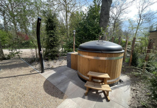 Outdoor photo of a round wooden hot tub with cover and stairs at a lodge in De Utrechtse Heuvelrug, Netherlands.