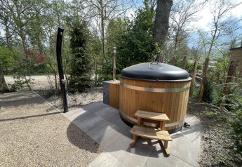 Foto all’aperto di una vasca idromassaggio rotonda in legno con coperchio e scaletta presso un lodge a De Utrechtse Heuvelrug, Paesi Bassi.