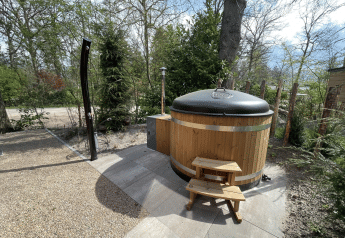 Bañera de hidromasaje redonda de madera con tapa y escalera en el exterior de un lodge en De Utrechtse Heuvelrug, Países Bajos.