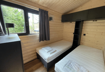 Moderne slaapkamer met twee enkele bedden, houten muren en raam in Hackfort Wood Hottub 6, De Utrechtse Heuvelrug.