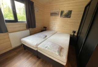 Bedroom with twin beds, wood-paneled walls, window, and artwork at Hackfort Wood Hottub 6, De Utrechtse Heuvelrug, Netherlands.