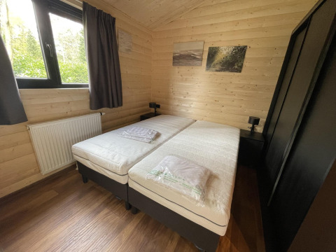 Dormitorio con dos camas individuales, paredes de madera y ventana en Hackfort Wood Hottub 6, De Utrechtse Heuvelrug, Países Bajos.