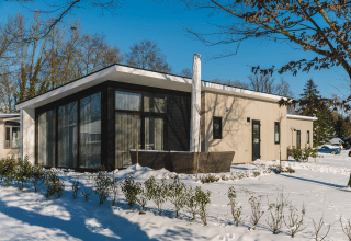 Bos Lodge ved Holiday Resort 't Schuttenbelt i Holland, moderne hytte med store vinduer omgivet af sne.