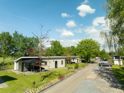 Bos Lodge op Holiday Resort 't Schuttenbelt in Nederland, omringd door groen en een heldere blauwe lucht.