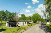 Bos Lodge op Holiday Resort 't Schuttenbelt in Nederland, omringd door groen en een heldere blauwe lucht.