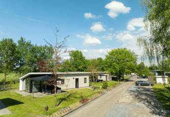 Bos Lodge im Ferienpark 't Schuttenbelt in den Niederlanden, umgeben von Bäumen und einem klaren Himmel.