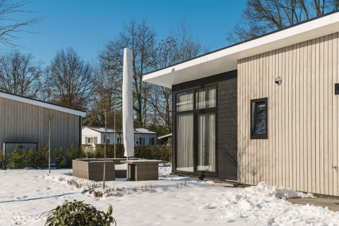 Moderne Bos Lodge bij Holiday Resort 't Schuttenbelt in Nederland, omringd door sneeuw en winters landschap.