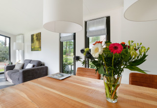 Sala en Bos Lodge del Holiday Resort 't Schuttenbelt, Países Bajos, jarrón de flores sobre mesa de madera.