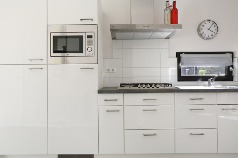Cocina blanca moderna con microondas integrado, fogón de gas y ventana en Bos Lodge, Países Bajos.
