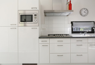 Cocina blanca moderna con microondas integrado, fogón de gas y ventana en Bos Lodge, Países Bajos.