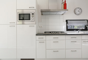 Moderne, hvidt køkken med indbygget mikroovn, gaskomfur, emhætte og vindue i Bos Lodge i Holland.